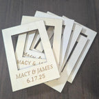 Several personalized mini wood photo frames fanned out, engraved with a custom name and date for a wedding favor.