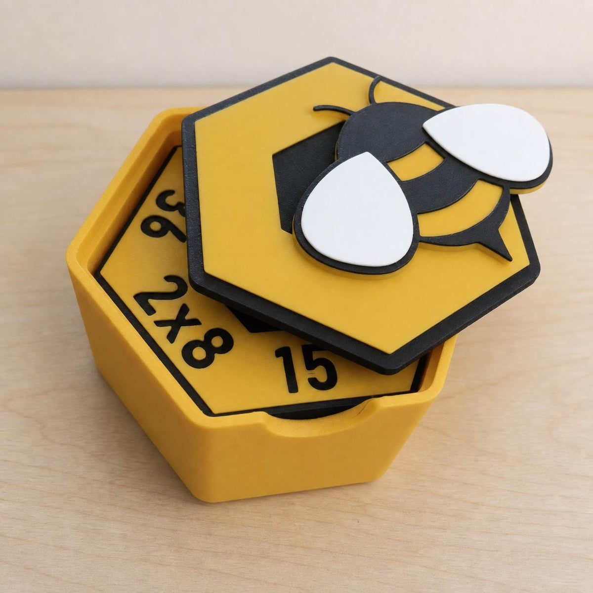 Open yellow HoneyHex storage box holding stacked multiplication tiles with the bee-decorated lid resting across the top.
