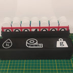 Open black storage case holding the three colored metric boards, with white volume, length, and mass icons visible on the lid.
