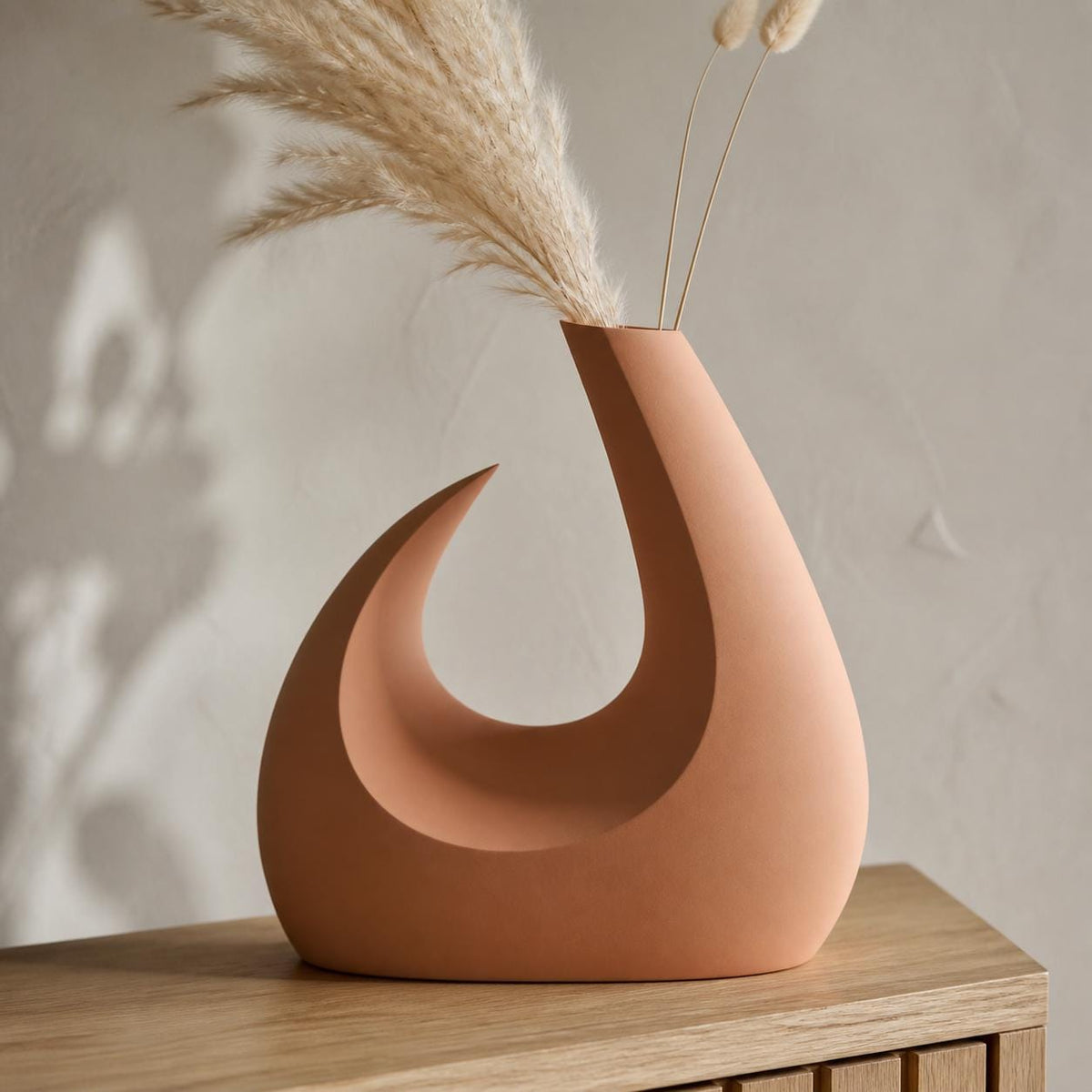 Close-up lifestyle view of the Solstice Arc vase in Terracotta with dried stems