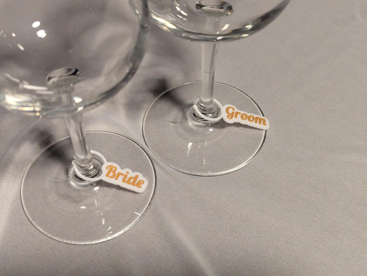 Close-up side view of bride and groom name charms resting around two wine glass stems.