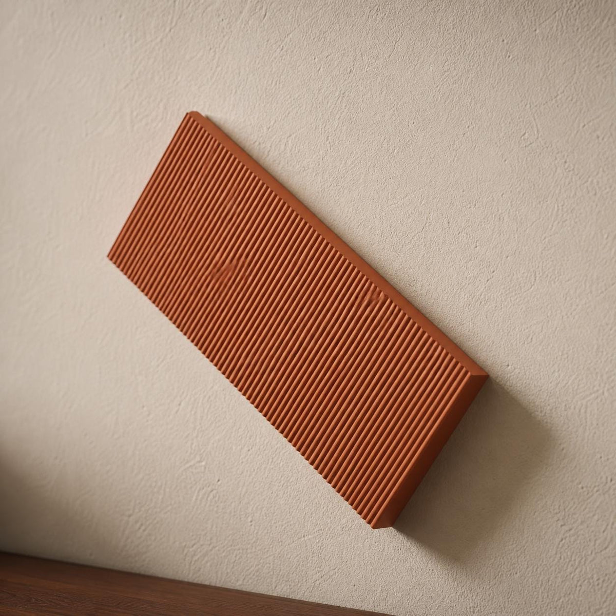 Close-up Terracotta RidgeLoom geometric wall tile mounted diagonally above a walnut console