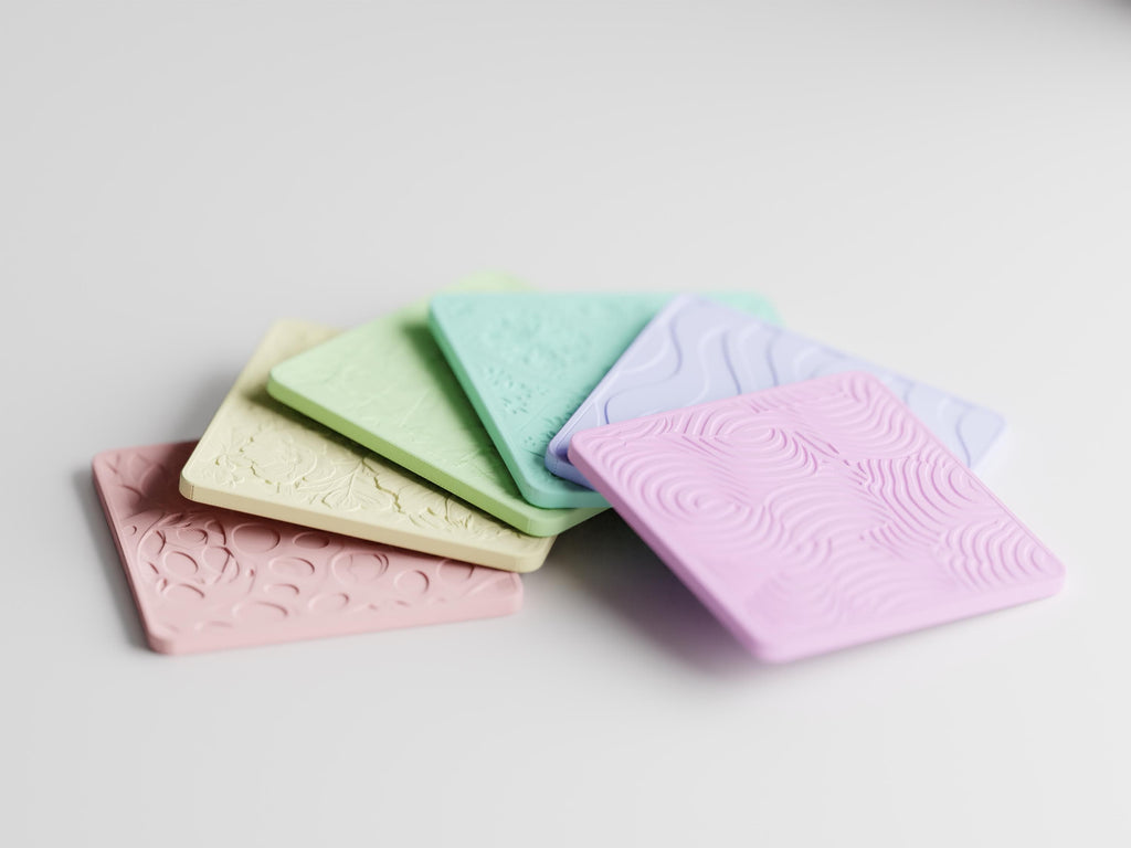 Low-angle close-up of the six TactileBloom patterned coasters in the fixed pastel assortment