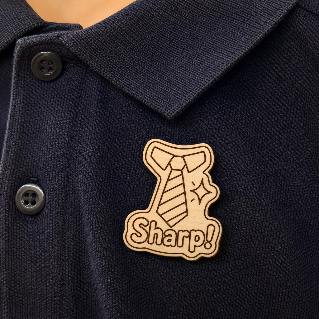 Dapper Day Sharp engraved birch reward badge shown close up in a realistic meeting setting.