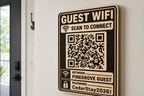 Bold Connect Guest WiFi Sign engraved birch sign mounted on a realistic neutral interior wall from a close side angle in natural birch and dark engraving, showing the QR code and guest network details.