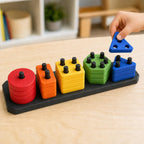 Child's hand holding a blue three-hole triangle above the matching pegs of the Rainbow Trail ShapeHarbor learning puzzle on a wood table.