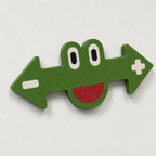 Close front view of one green frog marker with white eyes, black pupils, red smile, left minus symbol, and right plus symbol.