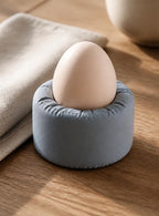 Morningswell egg cup in cool gray, three-quarter close-up on a breakfast table holding a shell-on egg.