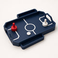 Close front-left view of the fully assembled RinkRush table hockey game in Dark Blue, Scarlet Red, and Ivory White on a warm white background