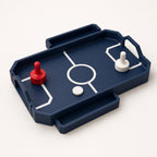 Close front-left view of the fully assembled RinkRush table hockey game in Dark Blue, Scarlet Red, and Ivory White on a warm white background