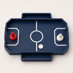 Near-overhead view of the Dark Blue RinkRush table hockey game with two attached catch trays, two pushers, and one Ivory White puck