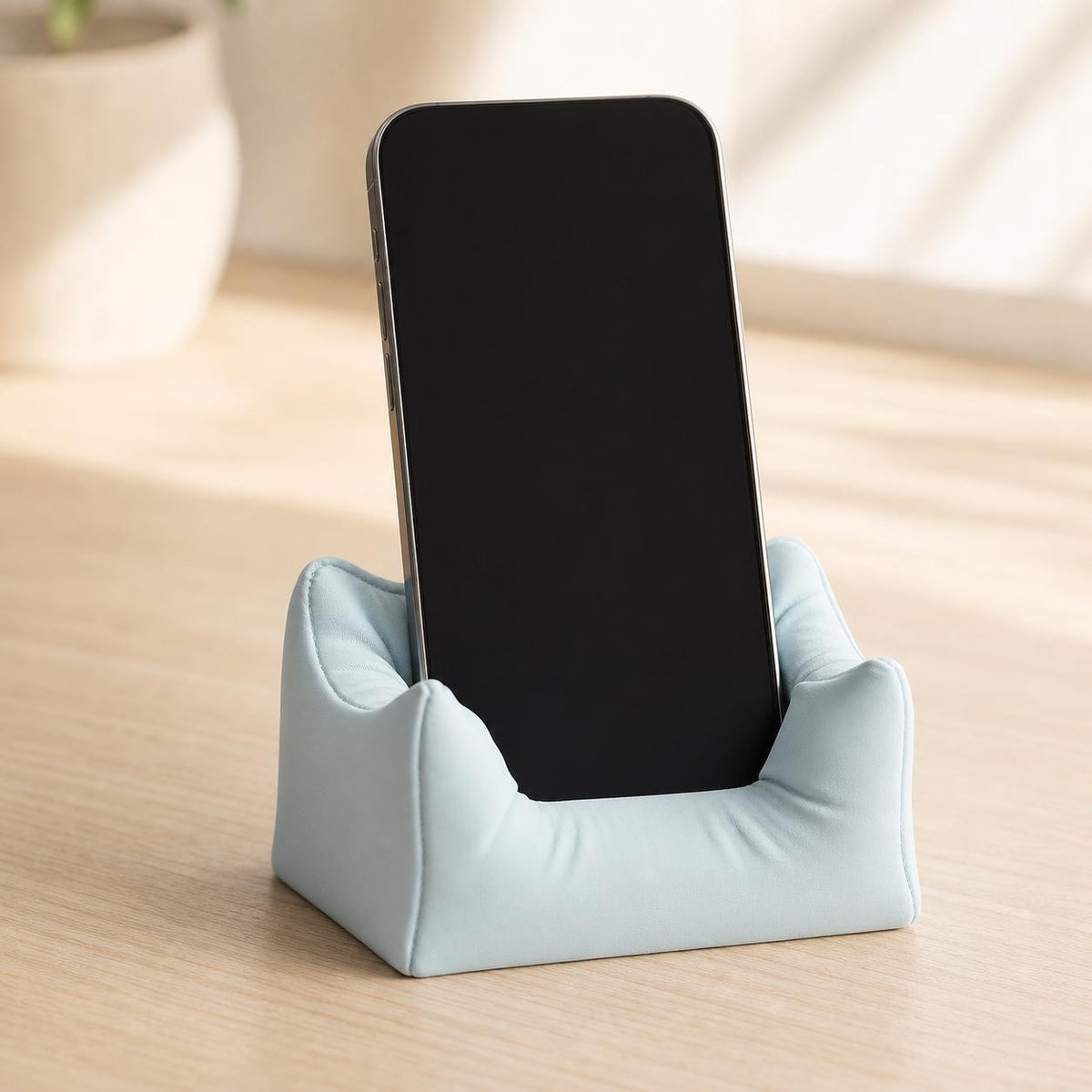 Close-up of the Plush Nook phone stand in Ice Blue holding a blank-screen smartphone
