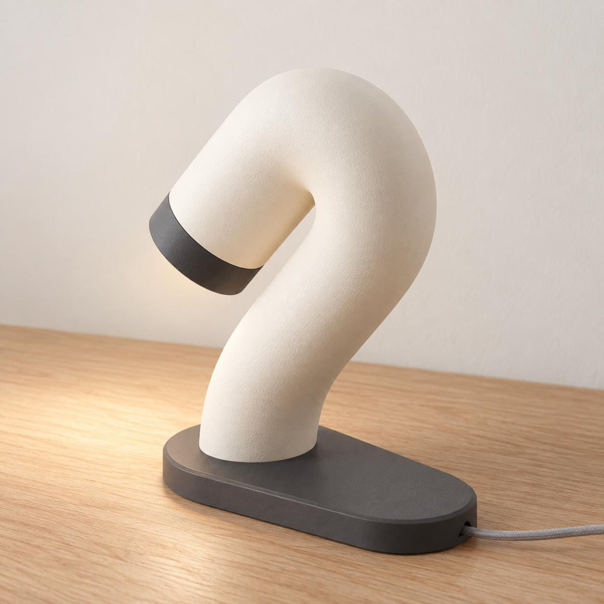 Rear three-quarter view of the Swayarc lamp in Ivory White and Charcoal, showing the flowing curve and cord exiting the oval base.