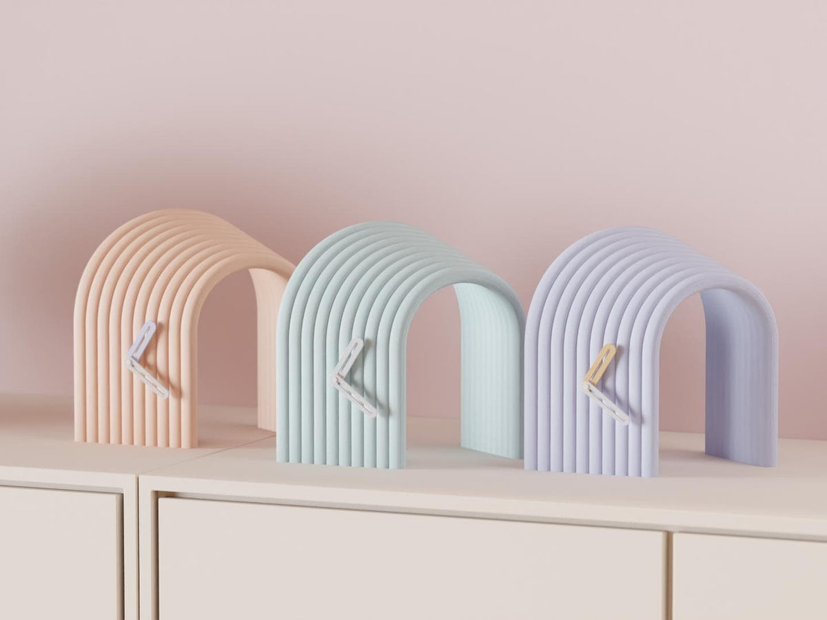 Arcspan Sculptural Desk Clock examples in contrasting colors on a pale cabinet, showing the finished clock faces and hands.