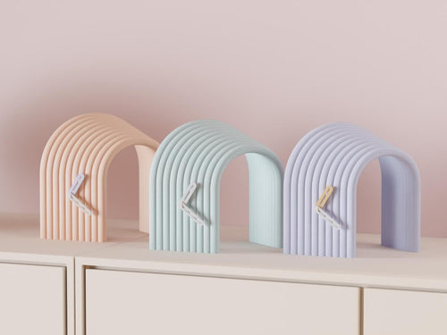 Arcspan Sculptural Desk Clock examples in contrasting colors on a pale cabinet, showing the finished clock faces and hands.