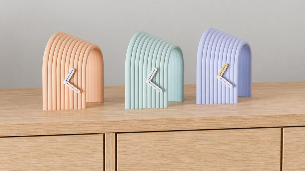 Alternate close-up of Arcspan Sculptural Desk Clock examples on light oak, showing their colored faces, hands and body profiles.