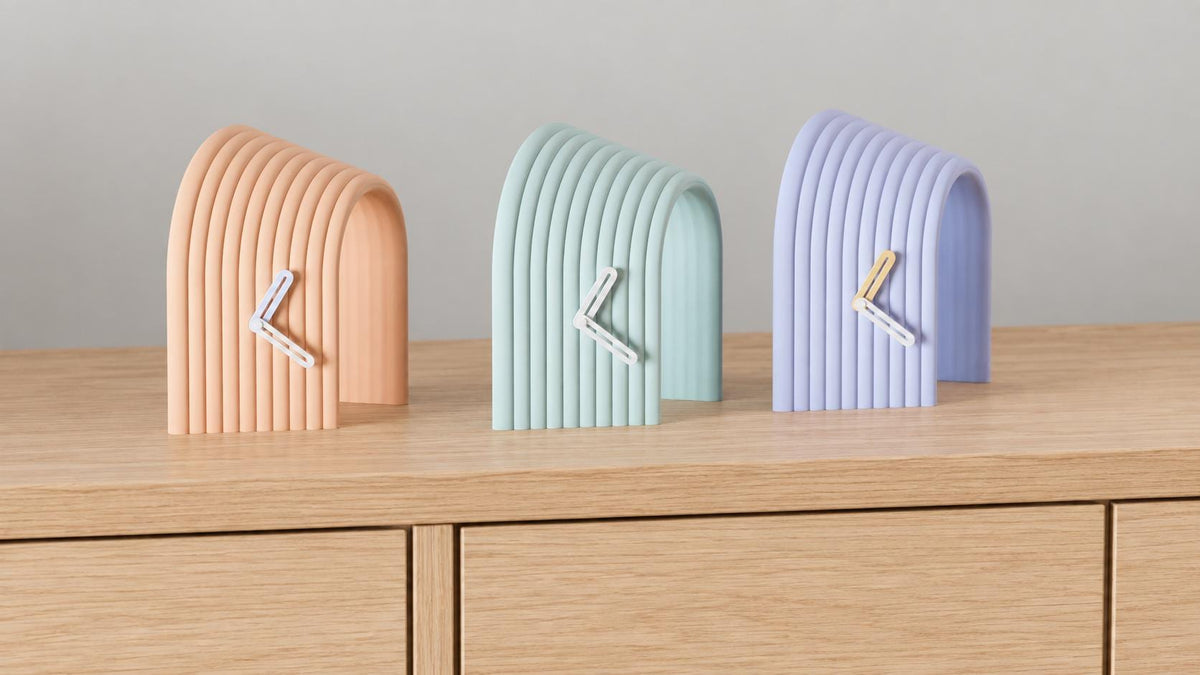 Alternate close-up of Arcspan Sculptural Desk Clock examples on light oak, showing their colored faces, hands and body profiles.