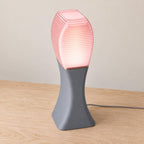 Elevated three-quarter view of the Arcelle lamp in Rose Quartz, with an Ash Gray matte base and Cherry Pink ribbed shade, power cord visible.