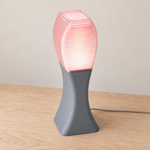 Elevated three-quarter view of the Arcelle lamp in Rose Quartz, with an Ash Gray matte base and Cherry Pink ribbed shade, power cord visible.