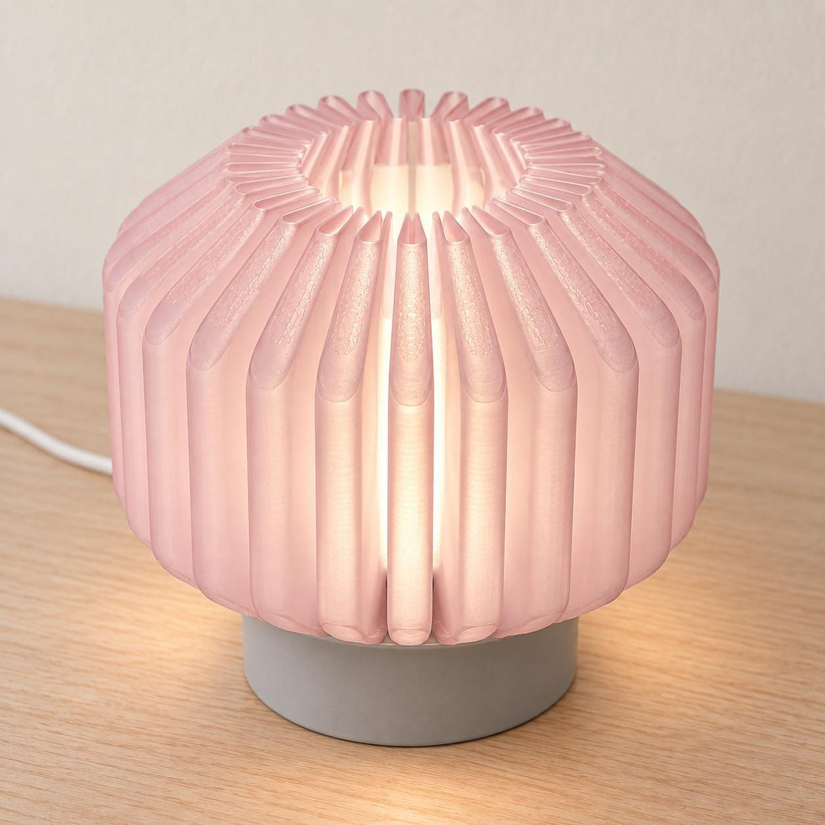 Elevated view of the Rose Mist Orivelle lamp showing its Cherry Pink folded ribs, open top, neutral inner diffuser, Ash Gray base and white cord.