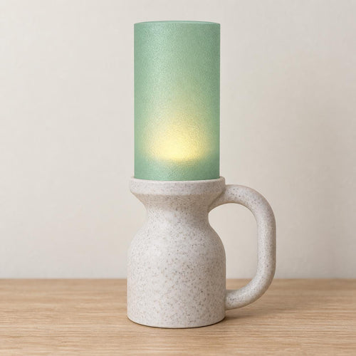 Alpine Jade Avelune lamp with a White Marble speckled base and loop handle, Light Jade cylindrical shade and soft tea light glow on a wood tabletop.
