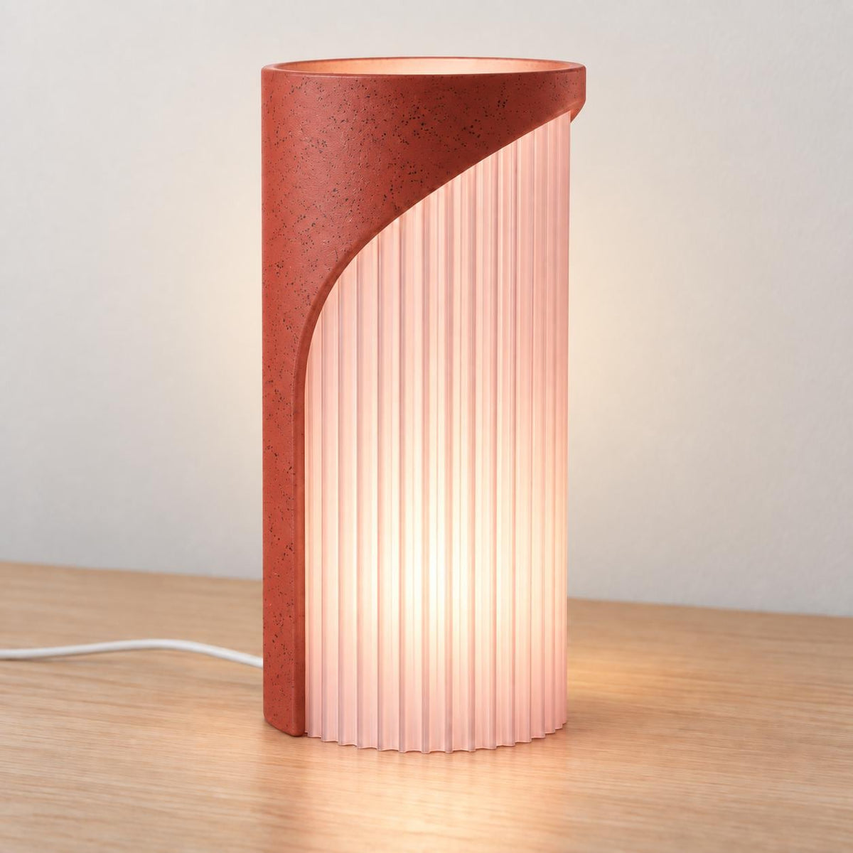 Granite Rose Caldora lamp with a Red Granite speckled back/top and glowing Cherry Pink ribbed diffuser extending to the tabletop.