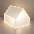 Three-quarter view of the illuminated Pagehaven frosted white lamp without a book, showing the continuous pitched shell and textured surface on a wood tabletop.