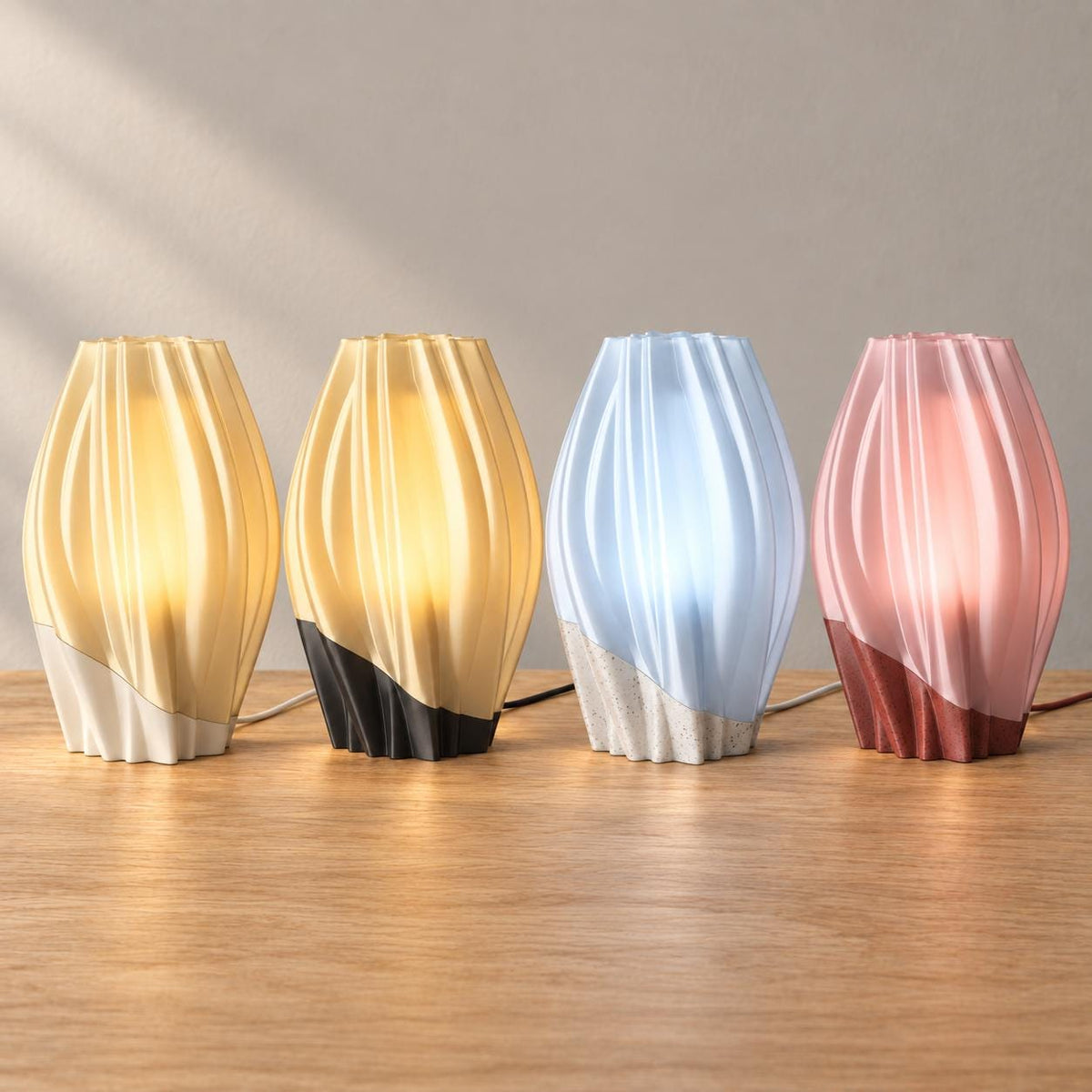 Four wired Orelune lamps on oak, left to right: Linen Halo, Midnight Amber, Marble Mist and Granite Blush, with flowing shades and curved base seams.