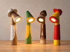 Four dressed character lamps in tan and white, green and yellow, tan and brown, and yellow and red outfits, close-up three-quarter view on light oak against a pale gray wall.
