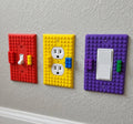 BuildBoard red toggle, yellow 2-Gang outlet, and purple rocker wall plates installed on a textured wall