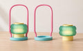Coral Cove lantern assembled beside an empty pink arched caddy and its intact teal ribbed light on a pale wood tabletop.