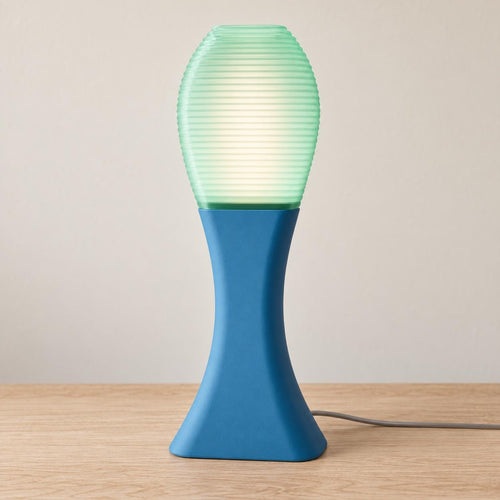 Tidal Mist Arcelle lamp with a Marine Blue matte base and glowing Light Jade ribbed shade on a pale wood tabletop, viewed from the front.