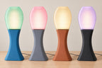 Four illuminated Arcelle lamps on a wood tabletop, left to right: Tidal Mist, Rose Quartz, Apricot Haze and Lilac Dusk.