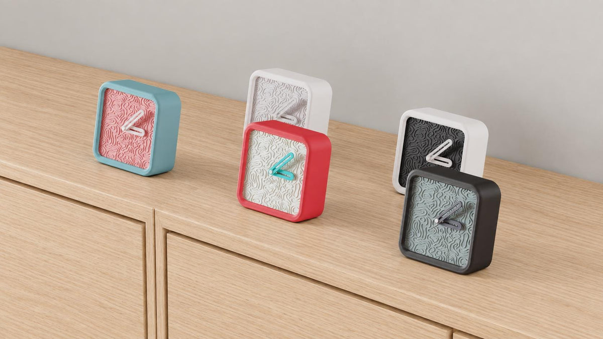 Angled close-up of Contourhour Desk Clock examples in contrasting colors on light oak against a gray wall.