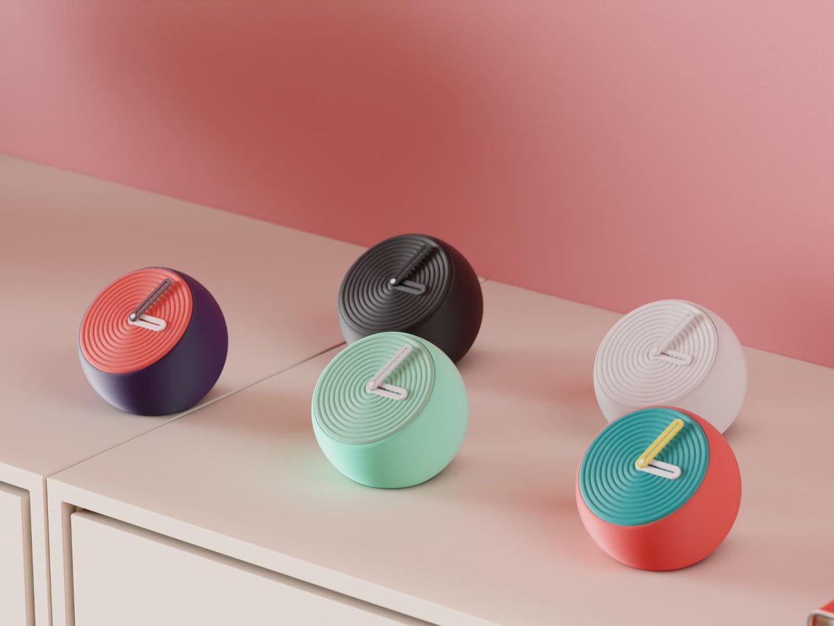 Pebblewave Spherical Desk Clock examples in contrasting colors on a pale cabinet, showing the finished clock faces and hands.