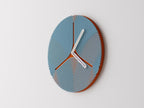 Triripple Wall Clock, blue curved ribs over a rust-colored round face with white hands, mounted on a pale wall in an angled view.