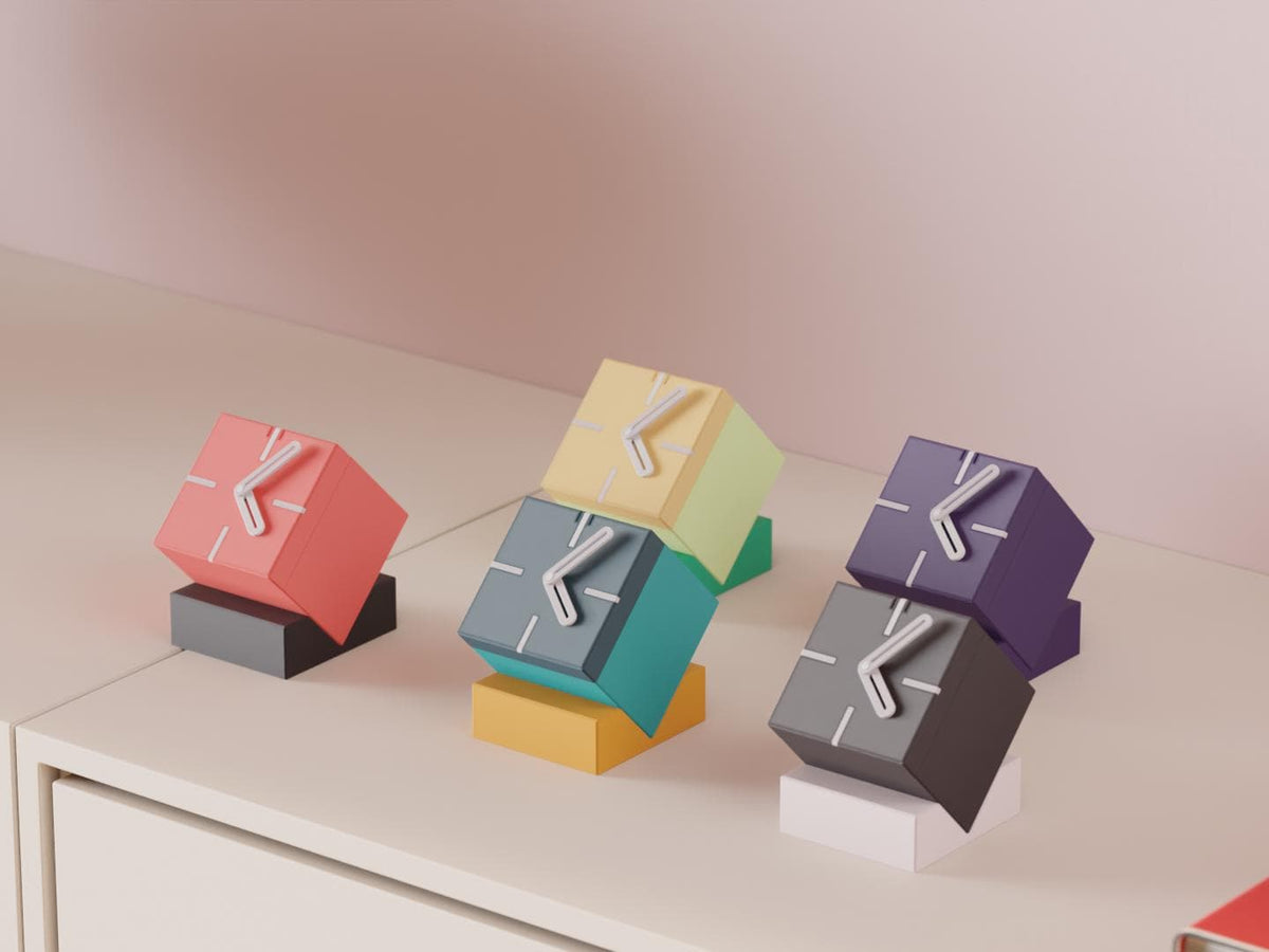 Tiltblock Cube Desk Clock examples in contrasting colors on a pale cabinet, showing the finished clock faces and hands.