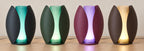 Four illuminated Lunafold lamps on a wood tabletop, left to right: Midnight Tide, Forest Mist, Plum Glow and Cocoa Amber.