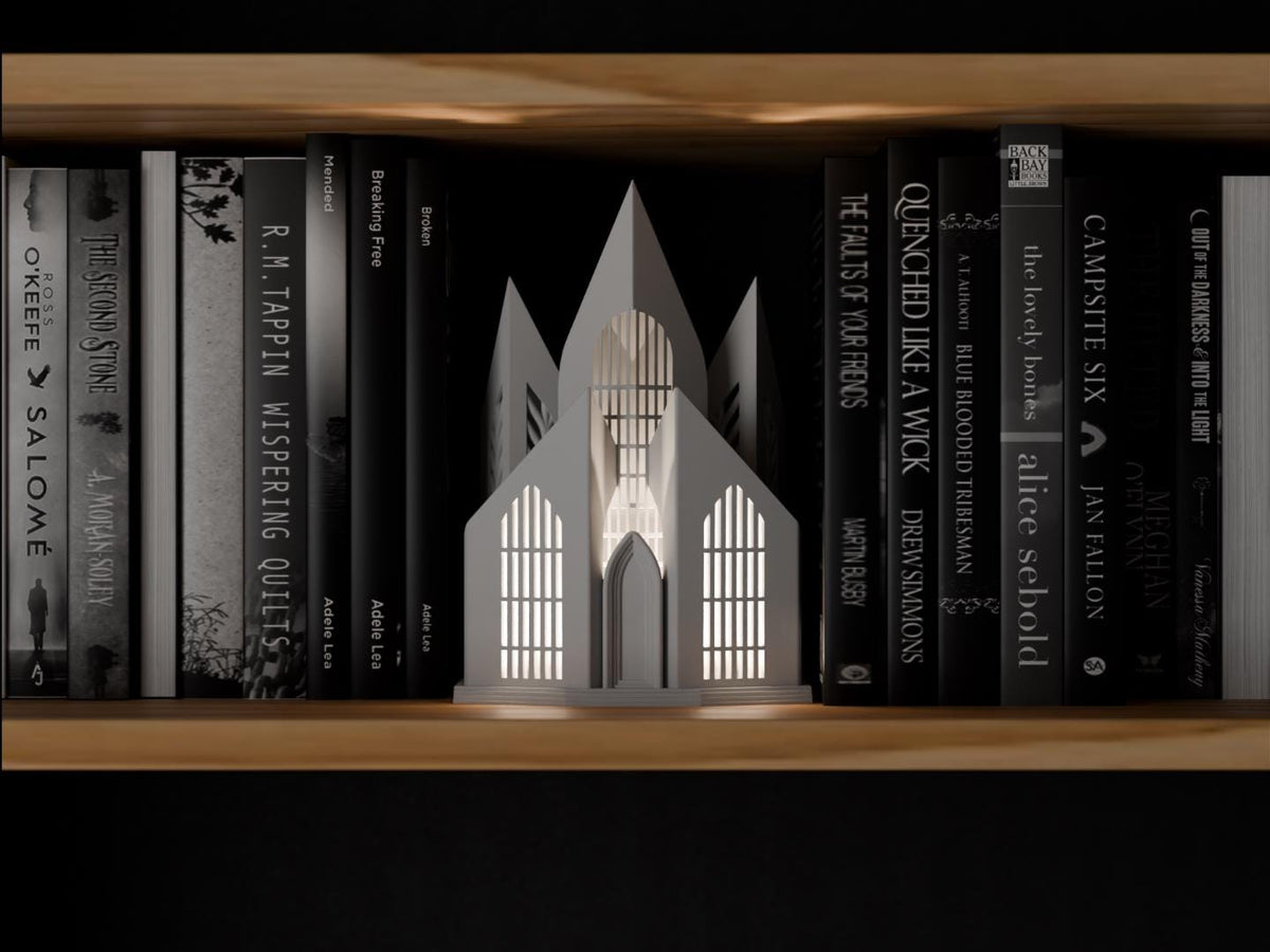 Quietspire Cathedral Book Nook in a light neutral color, shown from the front between books on a wooden shelf.