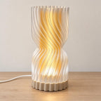 Amber Sand Rillora lamp with a Desert Tan matte base, glowing Mellow Yellow inner diffuser and clear rippled outer shade on a pale wood tabletop.