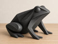 Charcoal frog sculpture, close-up main three-quarter view on pale oak against an ivory wall.