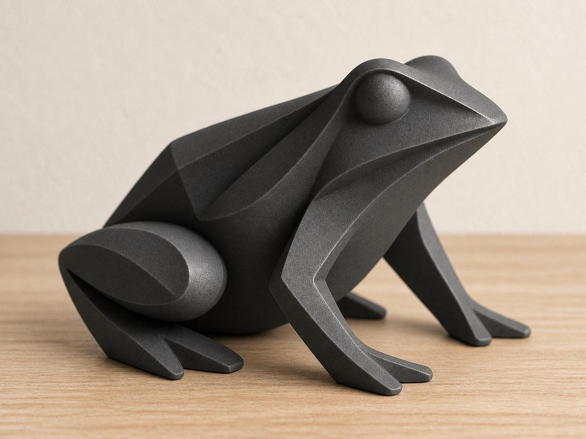 Charcoal frog sculpture, close-up main three-quarter view on pale oak against an ivory wall.