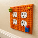 Close-up of an orange BuildBoard 2-Gang outlet wall plate installed with two duplex receptacles