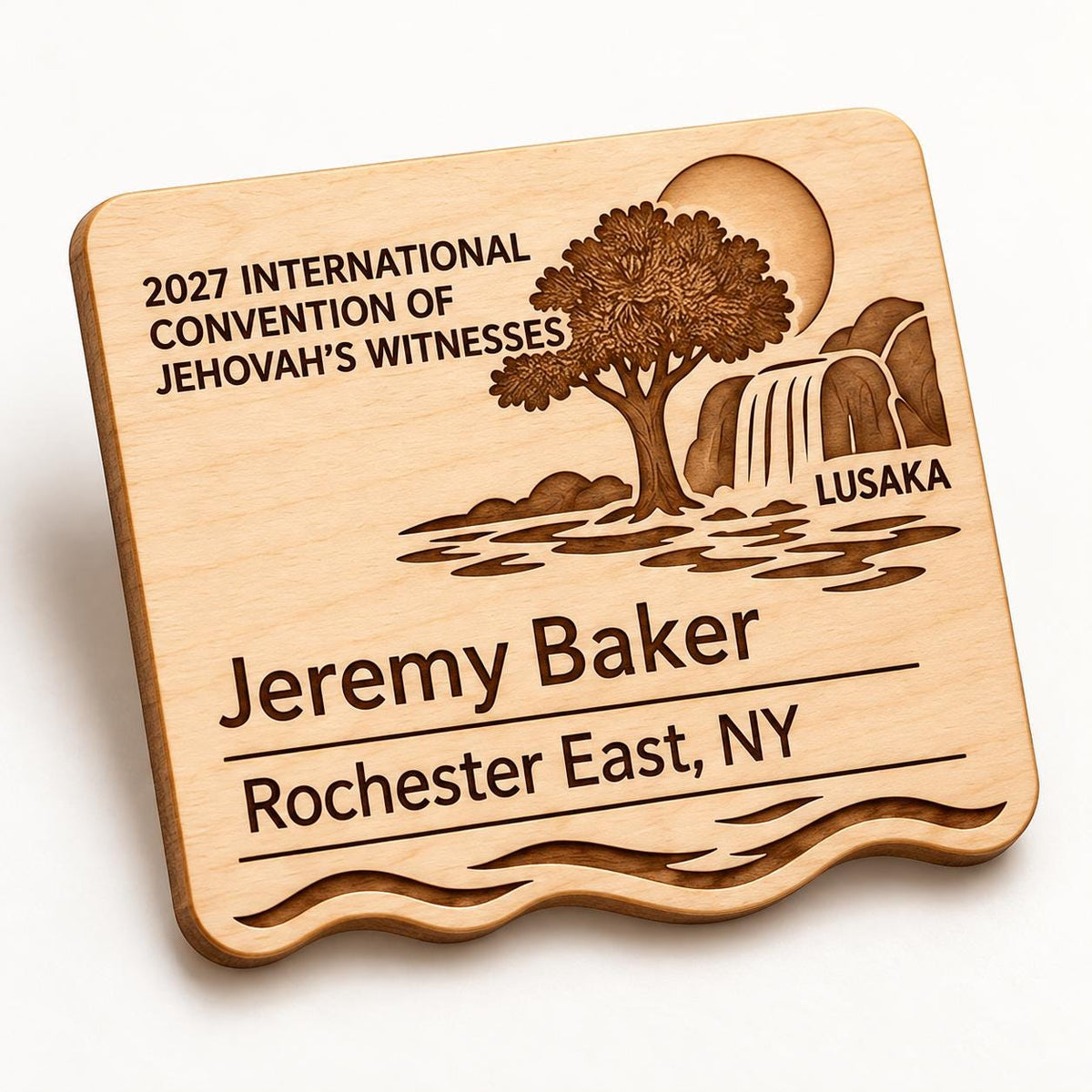 Oblique close-up of the Lusaka engraved natural-birch standard badge, showing its shaped edge and sample personalization on a white studio surface.