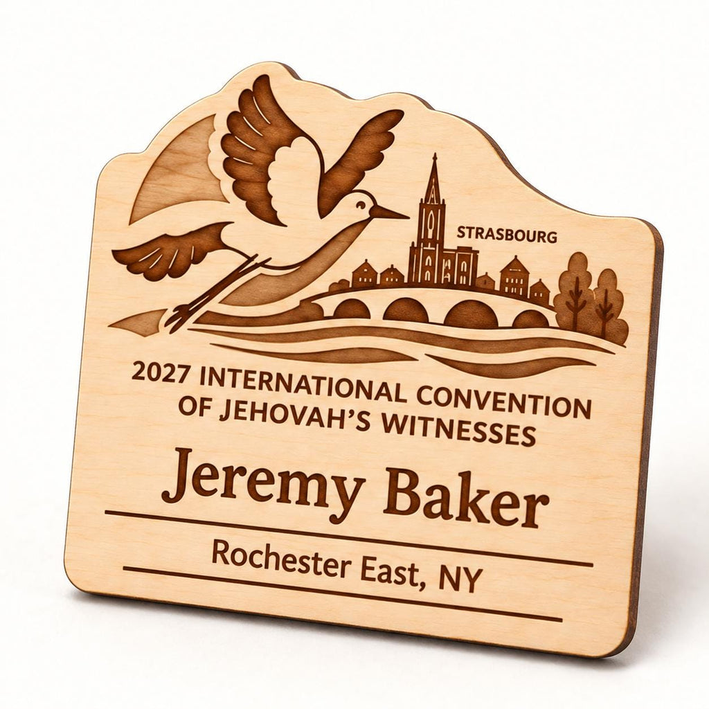 Oblique close-up of the Strasbourg engraved natural-birch standard badge, showing its shaped edge and sample personalization on a white studio surface.