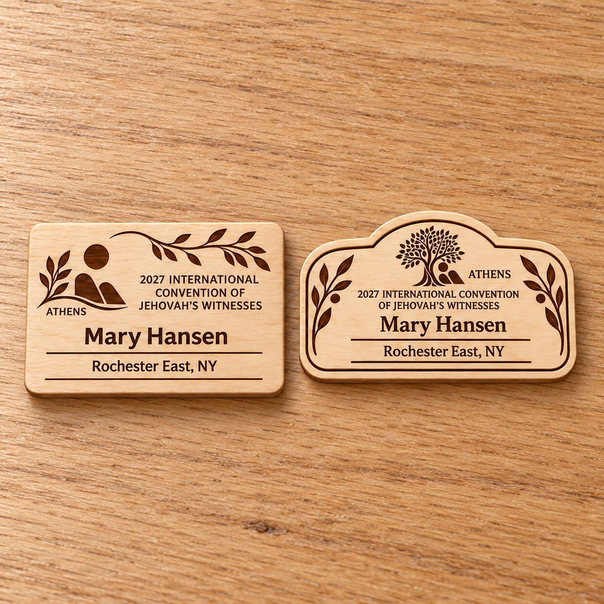 Two Athens mini natural-birch engraved badge designs, slot-free and laid separately on a light oak tabletop; each shows sample personalization.