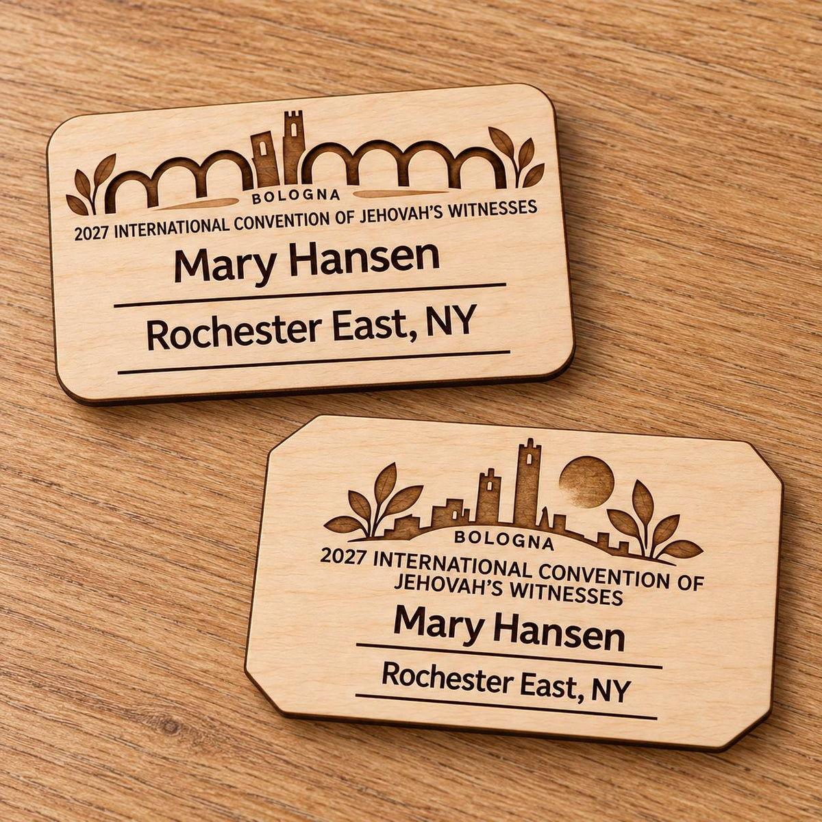 Two Bologna mini natural-birch engraved badge designs, slot-free and laid separately on a light oak tabletop; each shows sample personalization.