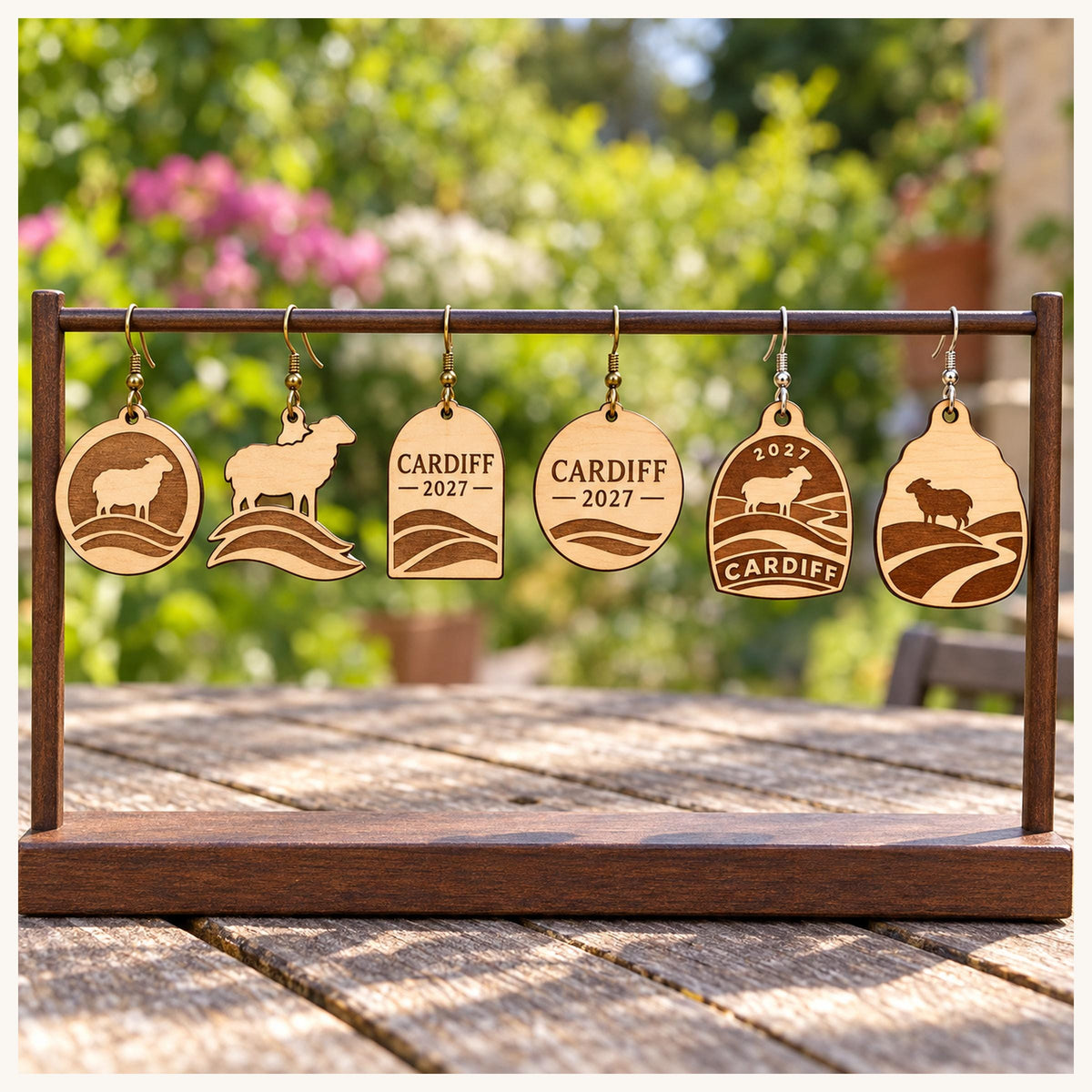 One earring from each selected Cardiff 2027 birch design on a wooden display stand outdoors.