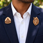 Two Abidjan engraved birch convention pin designs on the lapels of a navy man's suit outdoors.