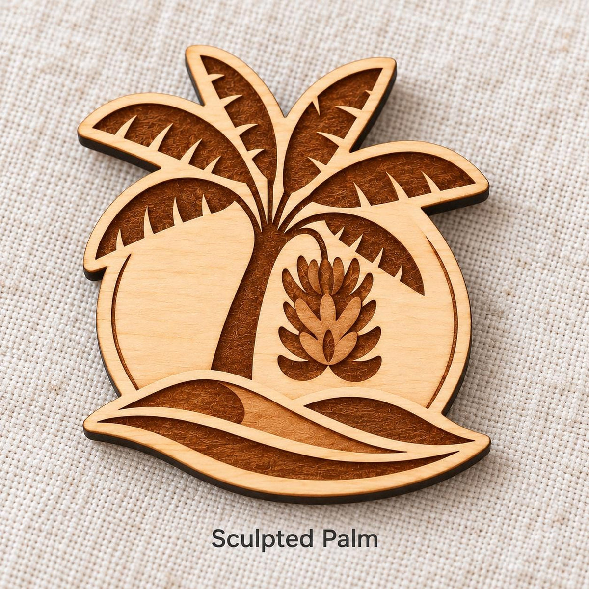Close-up of Gran Canaria Sculpted Palm engraved birch pin on linen, with design name caption.
